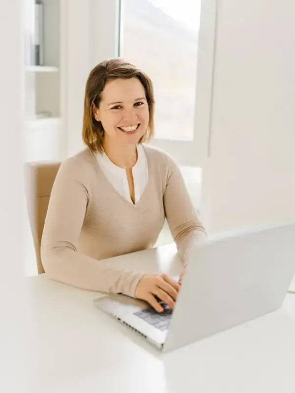 Denise Dewey-Muno lächelt in die Kamera in ihrem Büro. Es steht ein Laptop auf dem Tisch